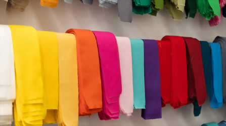 Farbig sortierte Stoffbahnen hängen in Reihen an der Wand einer Näherei und zeigen die Vielfalt der Materialien im textilen Ausbildungsbereich des Berufsbildungswerks Hettstedt.