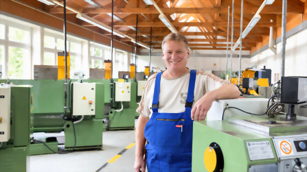 Ausbilder steht in der Metallwerkstatt zwischen Maschinen und Arbeitsplätzen.