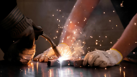 Schweißarbeit an Metall mit Schutz­handschuhen und Funkenflug in der Ausbildungswerkstatt.