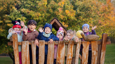 Kindergartenkinder Arche Kolping auf dem Außengelände winken in Kamera 