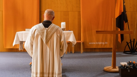 Pfarrer Hansch steht mit dem Rücken zu Gästen und betet 