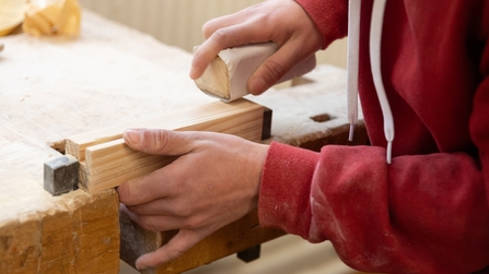 Junger Mann hobelt an Werkstück
