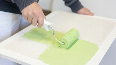Auszubildender bemalt eine Fläche mit grünger Farbe