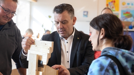 Teilnehmende der Inklusionswerkstatt erklären Mann den Bau eines Werkstücks